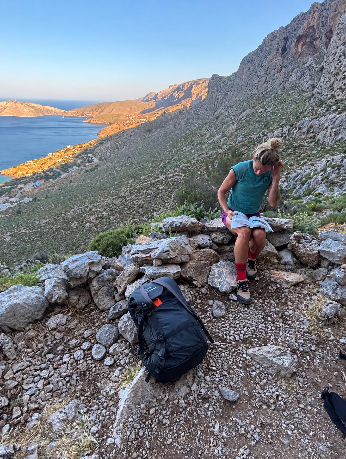 Sue reading on a rocky trail above the sea in Greece